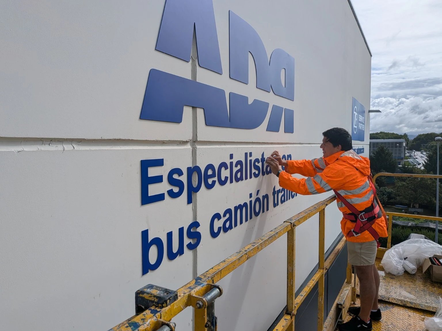 Instalación técnica de rotulación en altura sobre fachada industrial desde plataforma elevadora